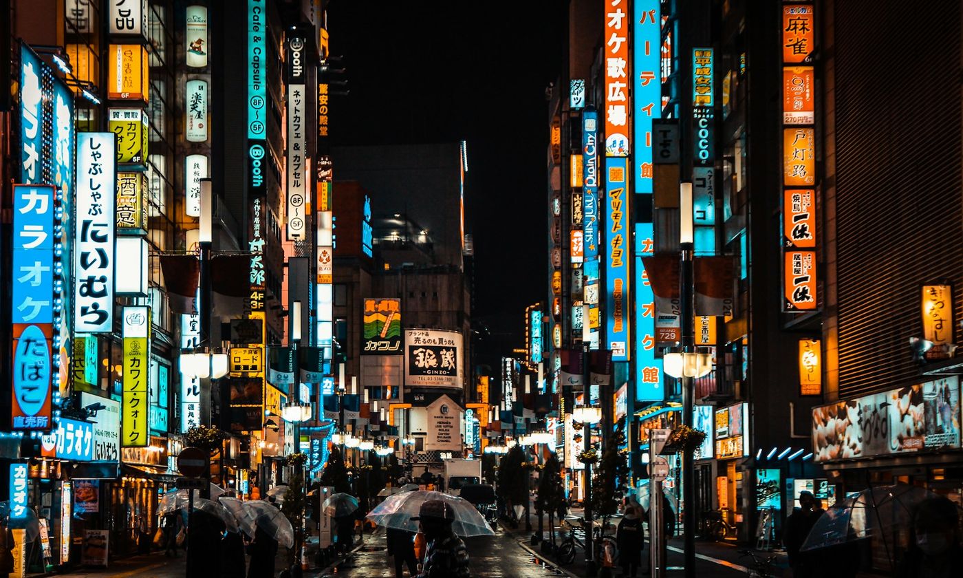 A rainy neon-lit Tokyo street at night seen past umbrellas
