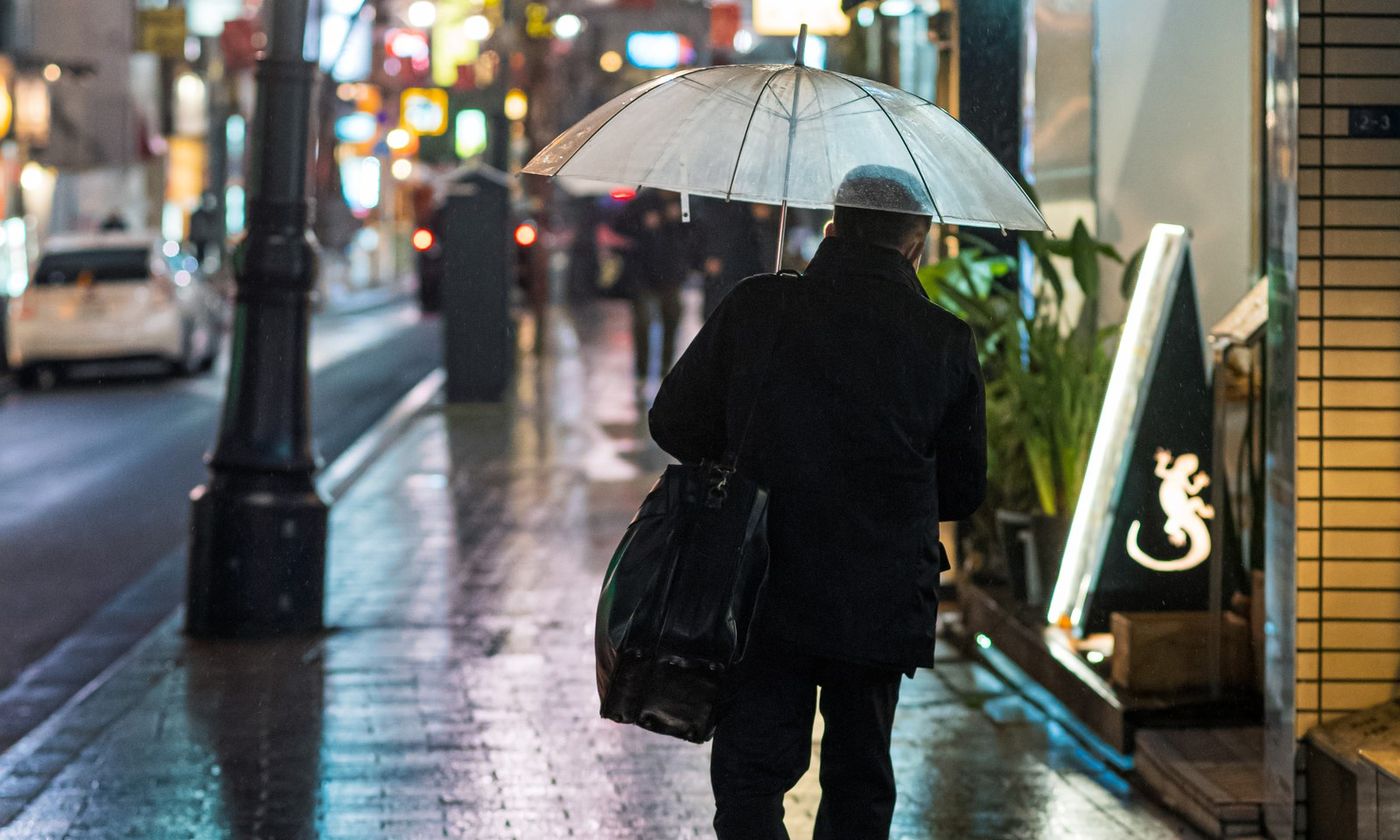 A person walking away under a clear umbrella on a wet neon-lit Tokyo street at night